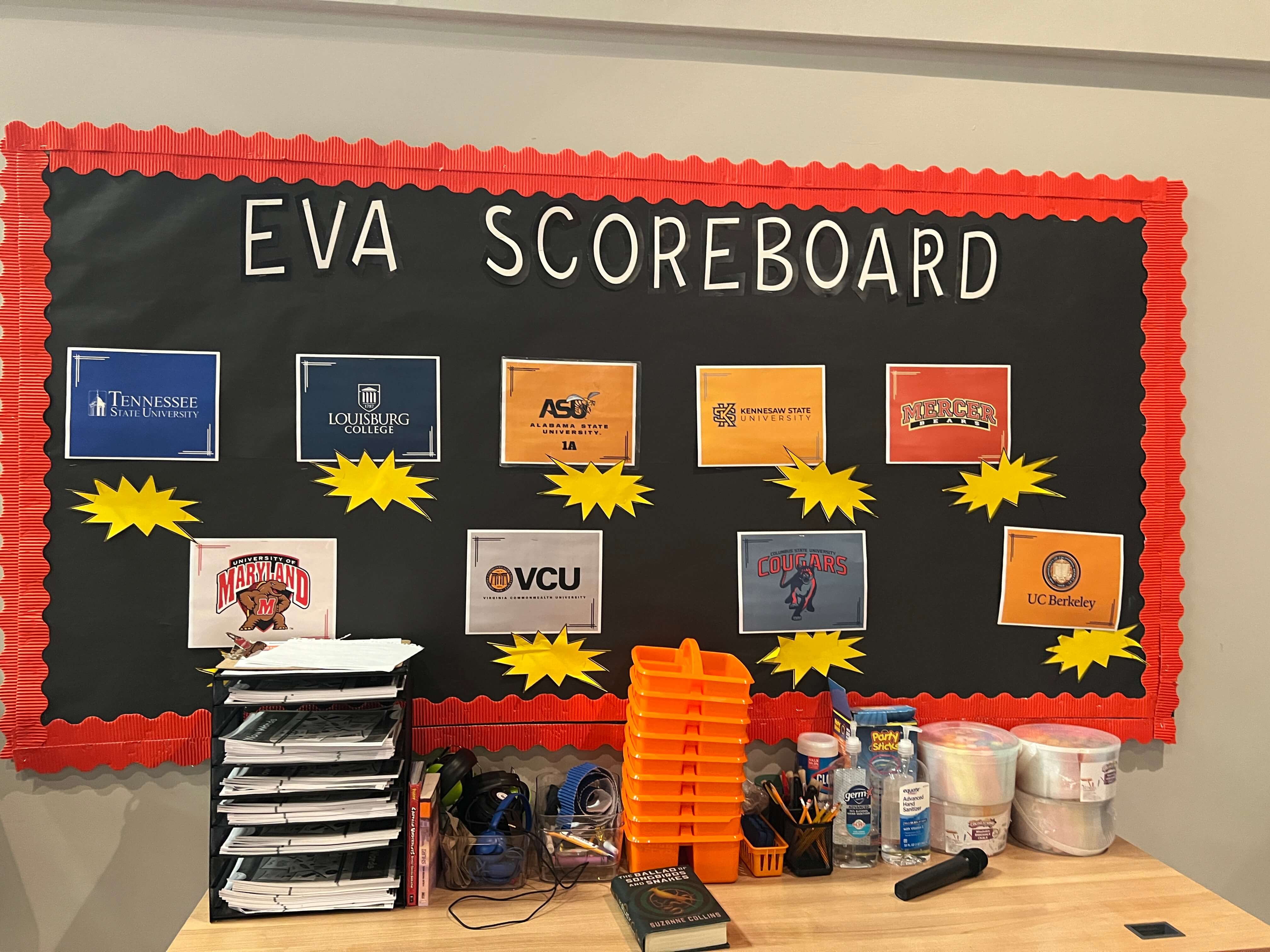 Classroom EVA scoreboard displaying college logos and student achievements with organized supplies below