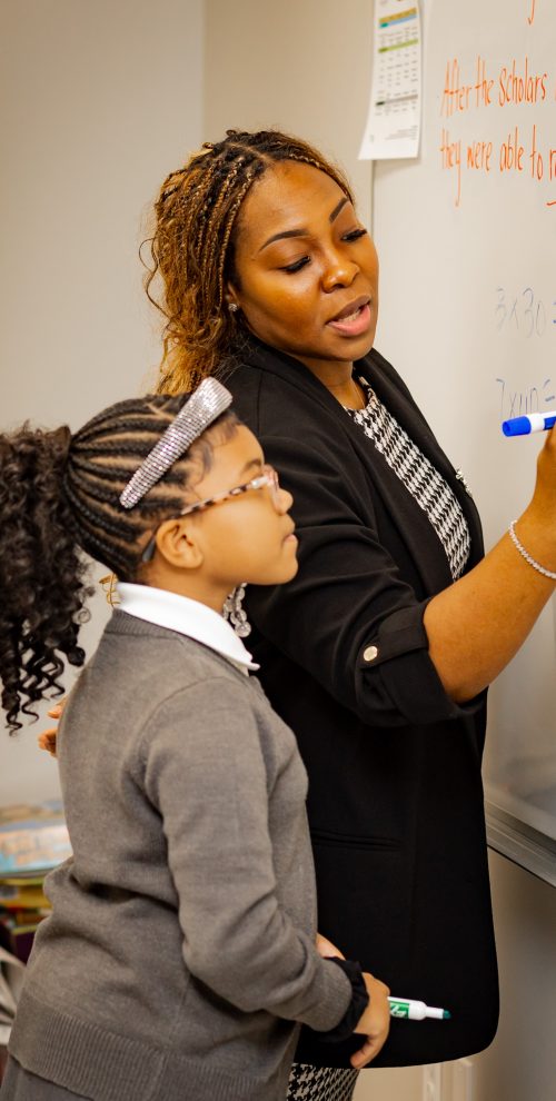 Teacher guiding student at whiteboard, writing lesson while student observes and learns